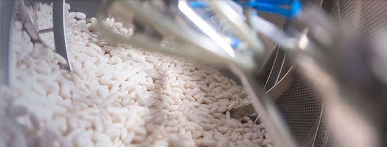 Weiße Kunststoffgranulate werden in einer industriellen Anlage über ein Fördersystem transportiert und weiterverarbeitet.