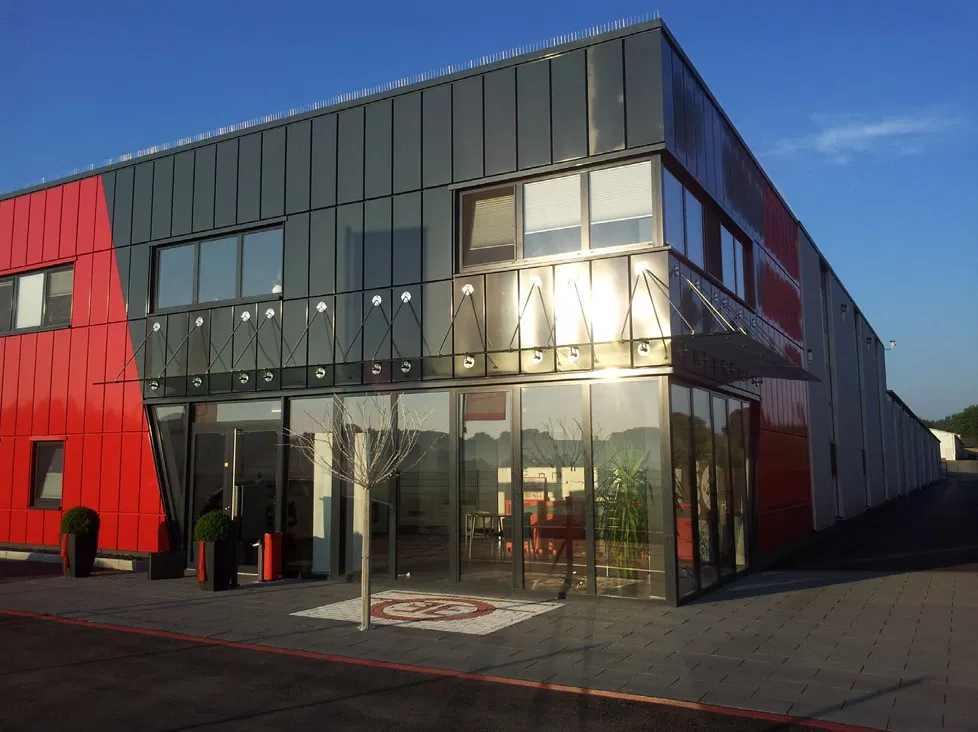 Modernes Firmengebäude mit Produktionshalle und Eingangsbereich bei sonnigem Wetter.